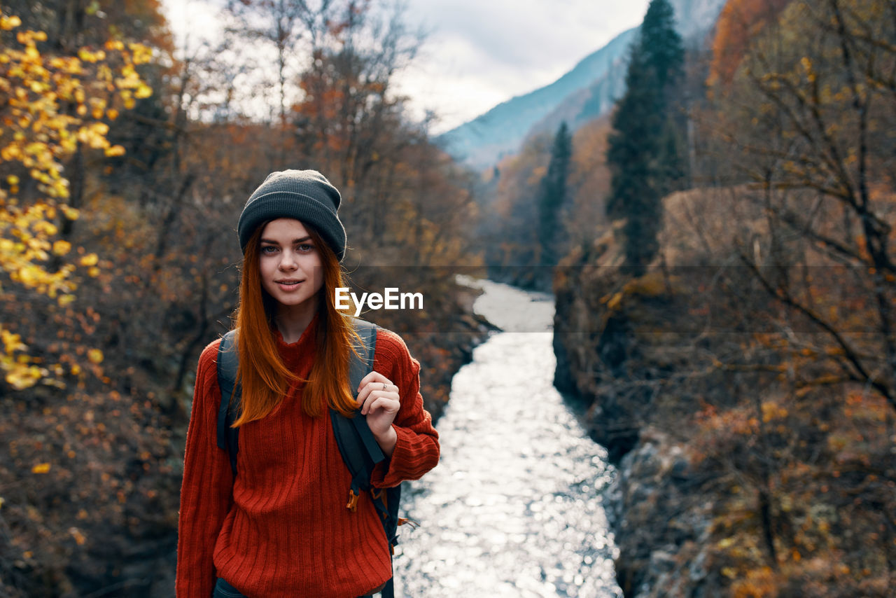 PORTRAIT OF SMILING YOUNG WOMAN STANDING BY TREE DURING WINTER