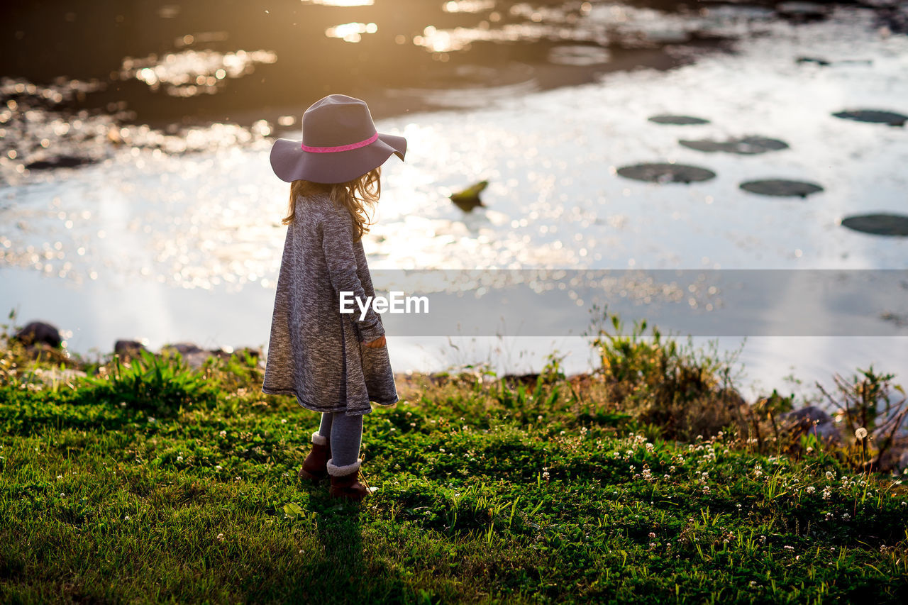 Side view of girl standing on grass by lake