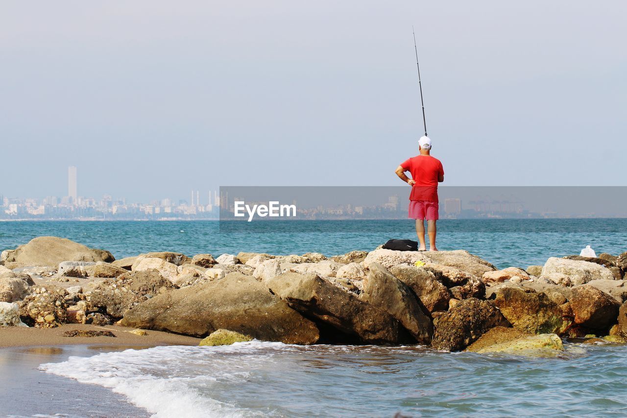 MAN FISHING ON ROCK AGAINST SEA