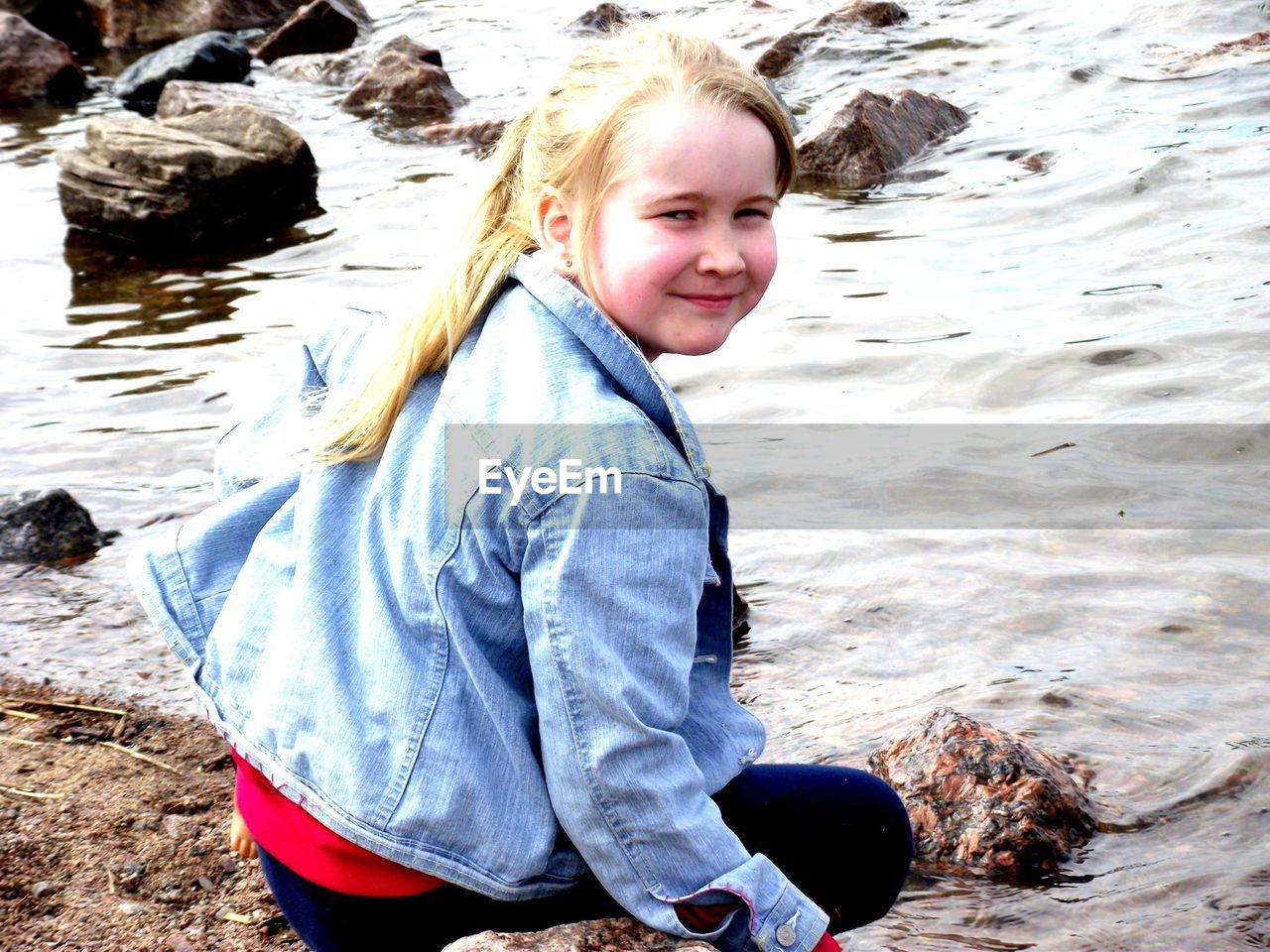 Smiling girl sitting on lakeshore on sunny day