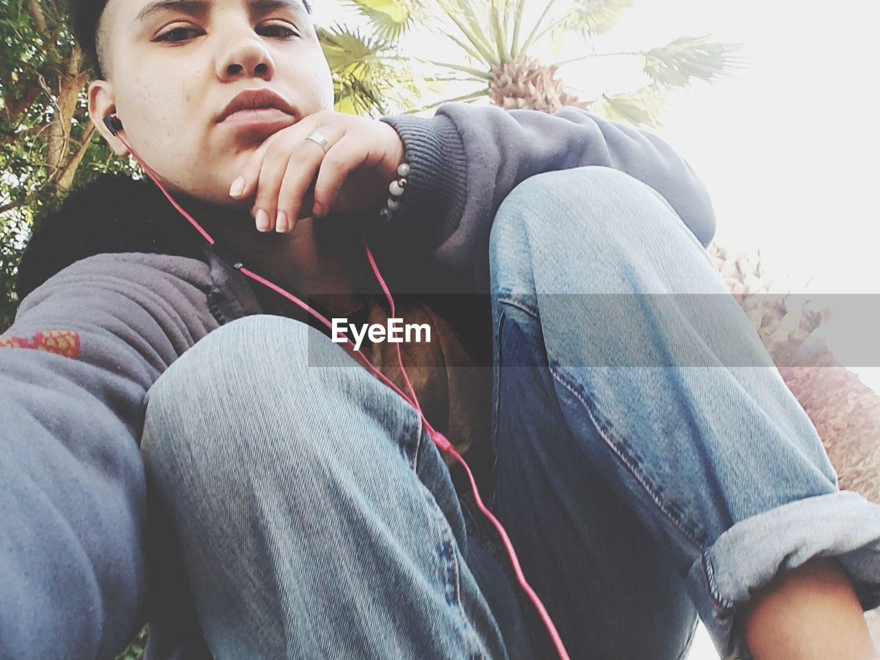 Low angle portrait of young man listening music while sitting by palm tree