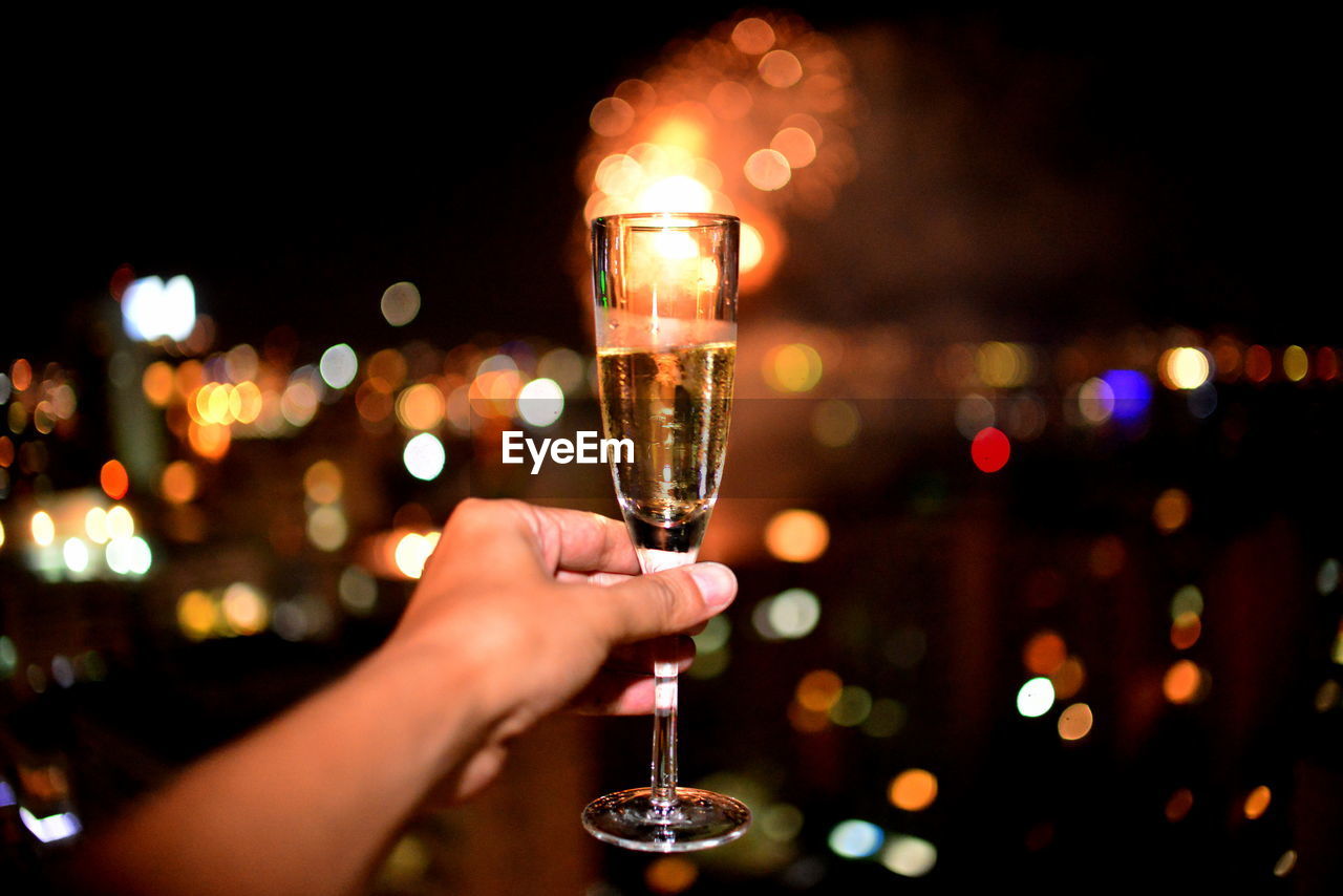 Close-up of hand holding champagne glass against fireworks