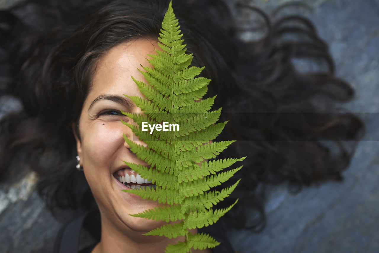 Woman with a fern on her face. she's lying on a rock and covers half her face with a fern leaf.