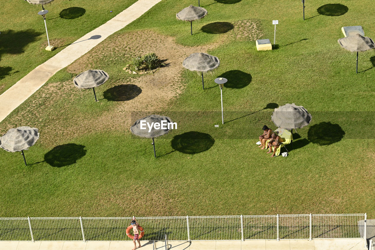 high angle view, grass, sports, leisure activity, group of people, men, nature, sport venue, green, day, screenshot, adult, plant, lifestyles, sunlight, outdoors, activity, aerial view, playground