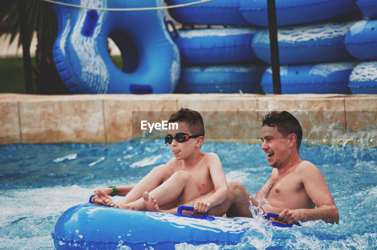 Happy father with son siting on inflatable raft in pool