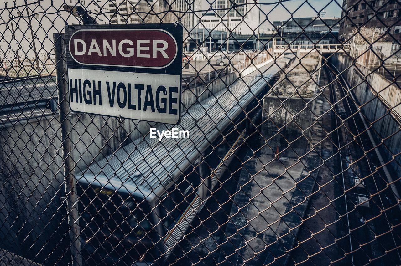 High voltage sign on chainlink fence by train in city