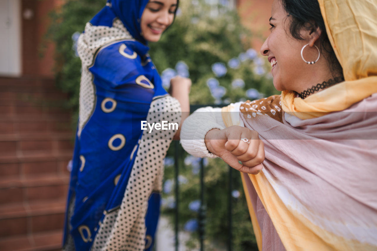 Smiling friends doing elbow bump while standing outdoors