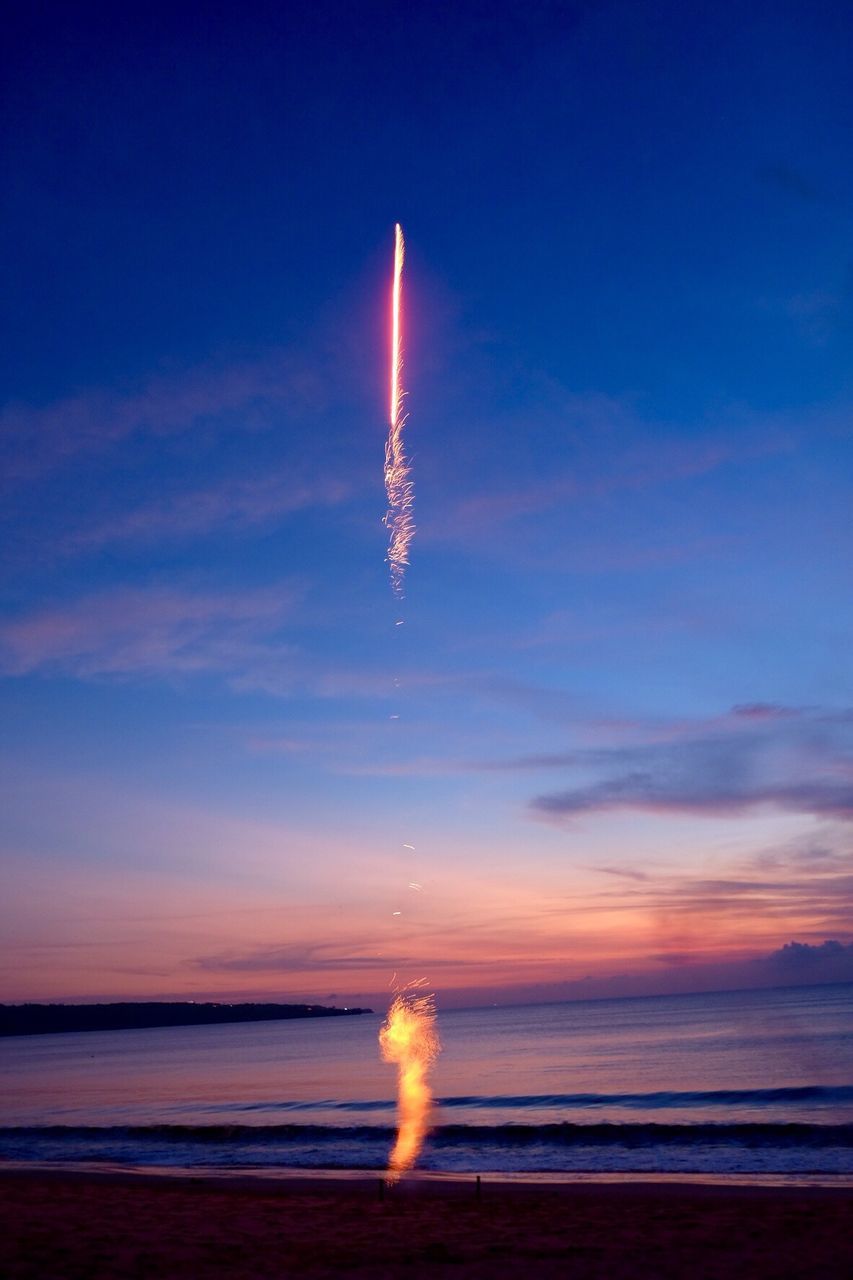 Firework exploding by sea against sky during sunset