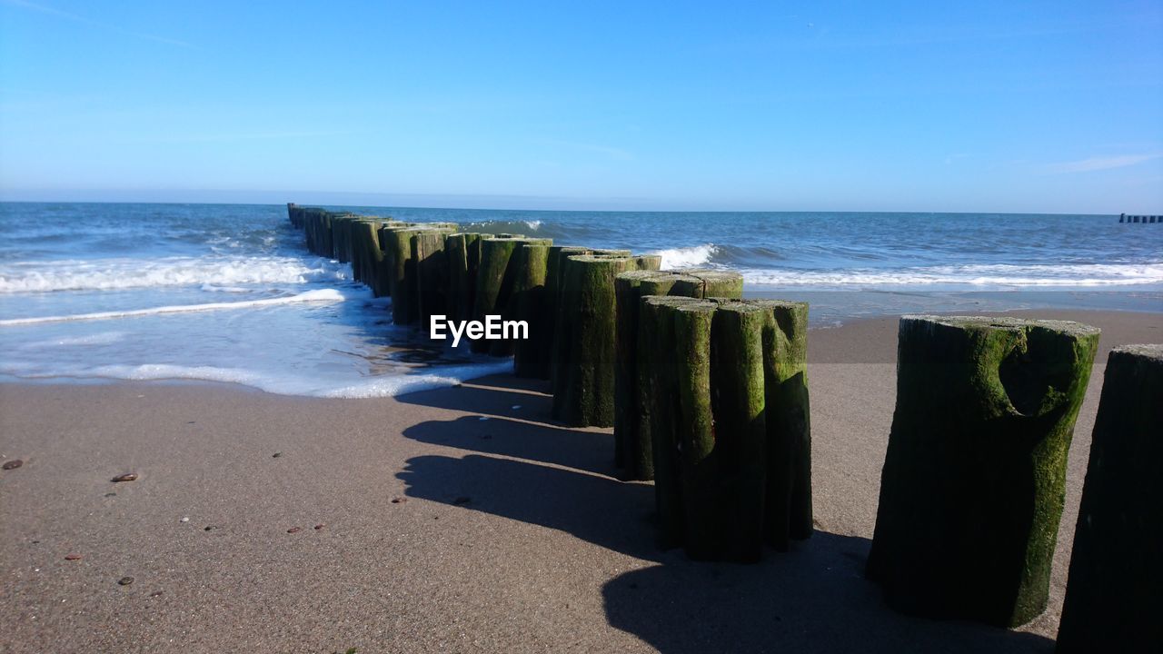 WOODEN POSTS ON BEACH BY SEA AGAINST SKY