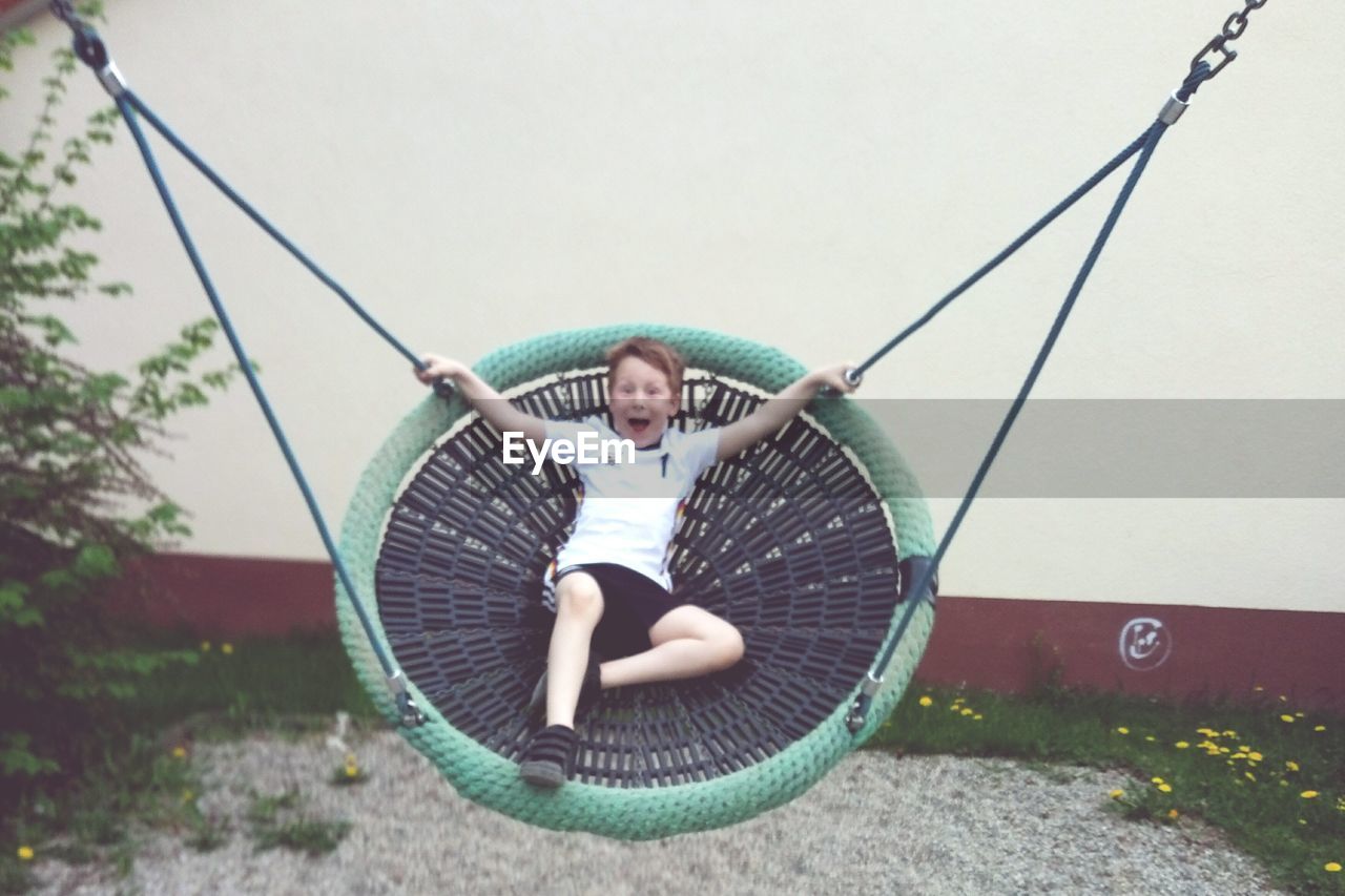 Portrait of playful boy enjoying on swing against wall