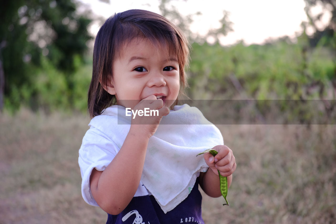 Portrait of cute girl eating bean while standing outdoors