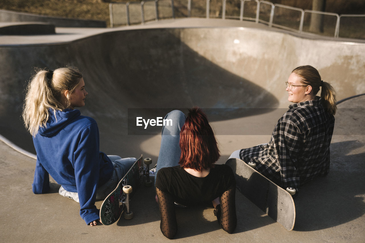 Teenage girls with skateboards sitting in skatepark