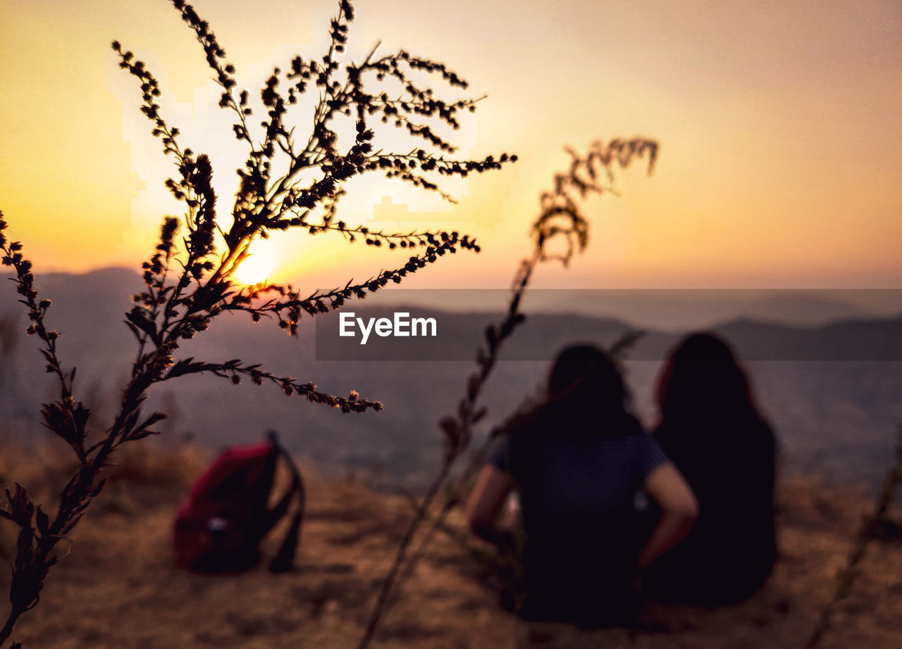 REAR VIEW OF SILHOUETTE COUPLE SITTING ON LAND DURING SUNSET