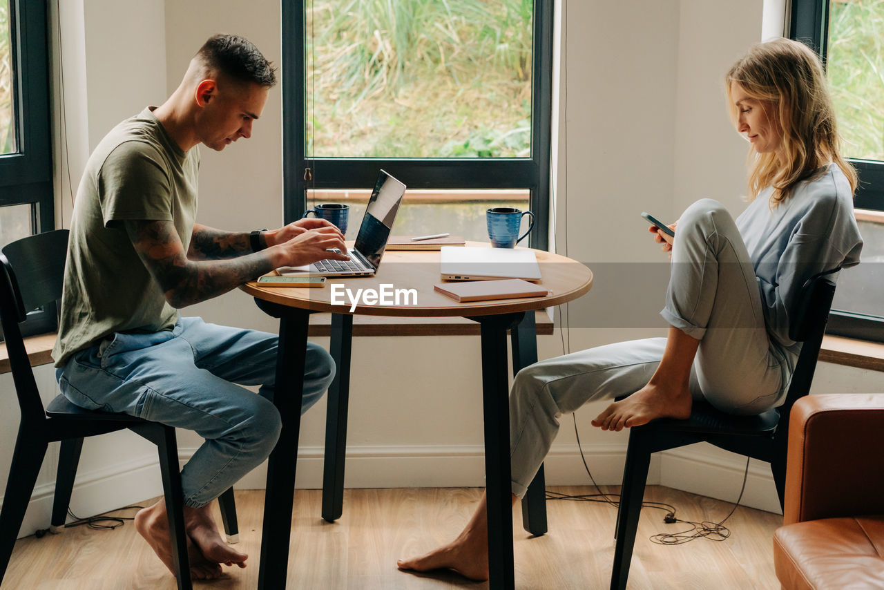 Businessman and businesswoman sit in an apartment and work on electronic devices in the living room