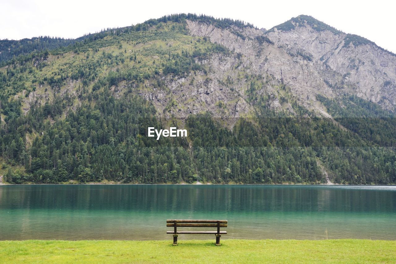 Empty bench by lake against mountain