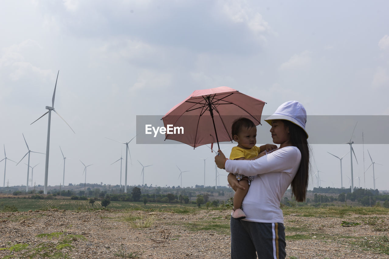 A young mother and her lovely little daughter are at a windmill field.