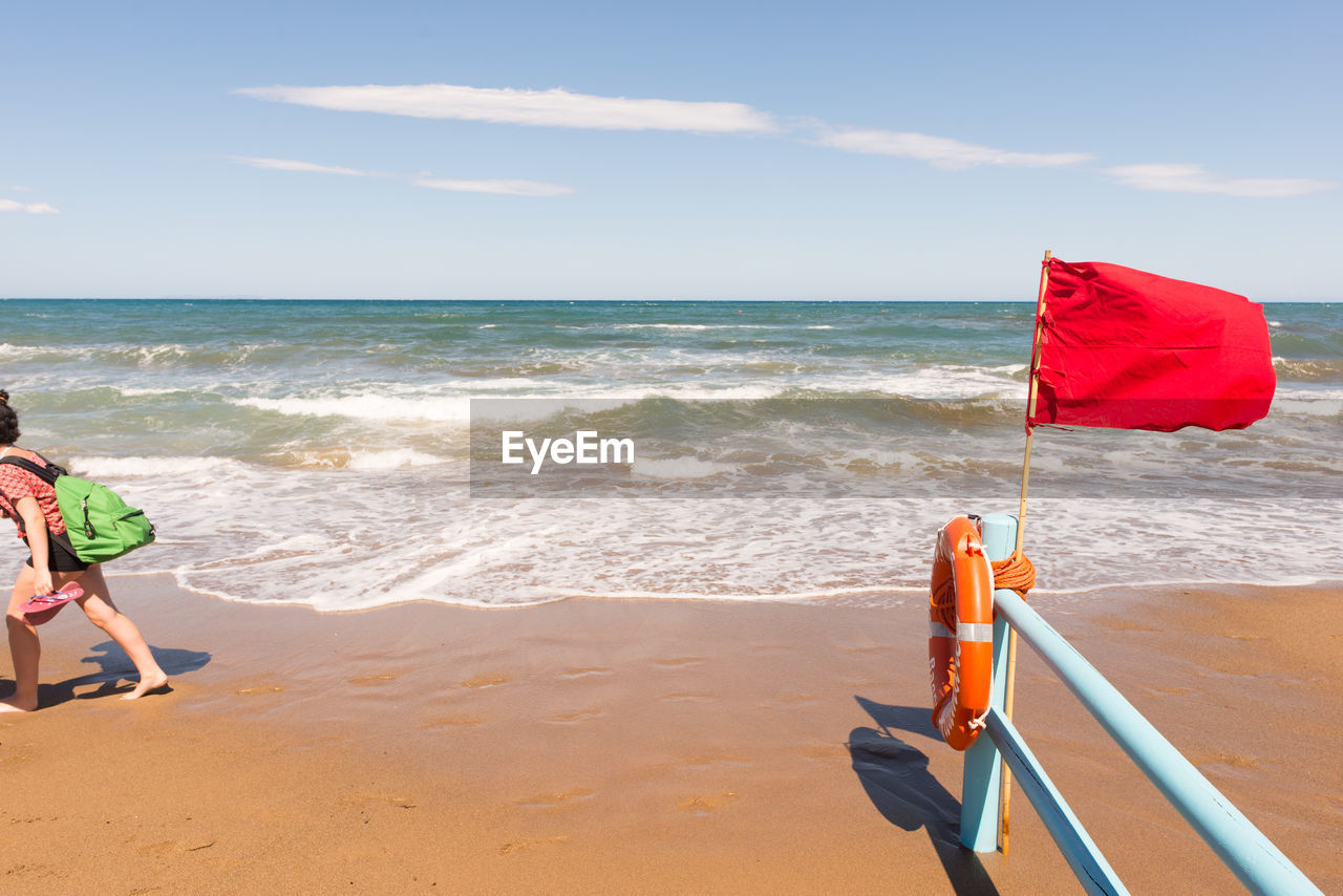 Side view of woman with backpack walking on shore at beach against sky