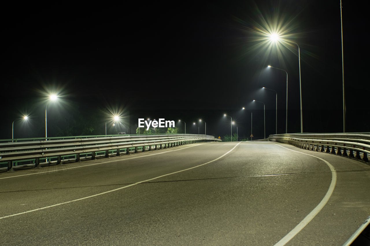 EMPTY ROAD ALONG ILLUMINATED STREET LIGHTS