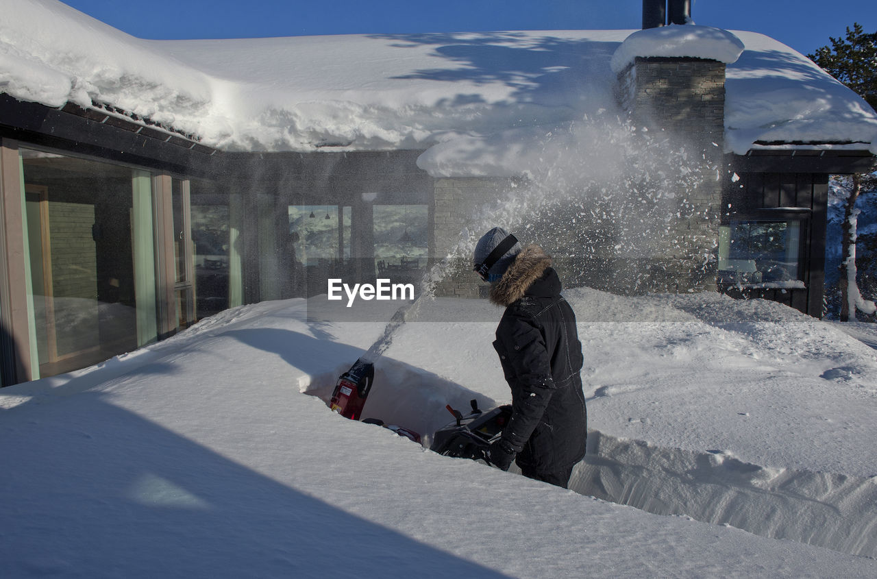 Man using snowblower by cabin during winter