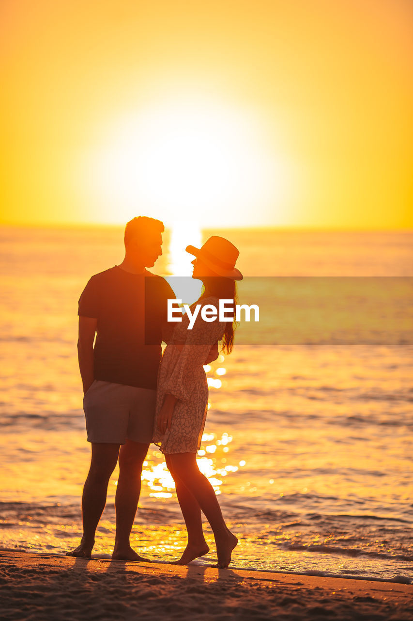 rear view of couple standing at beach during sunset