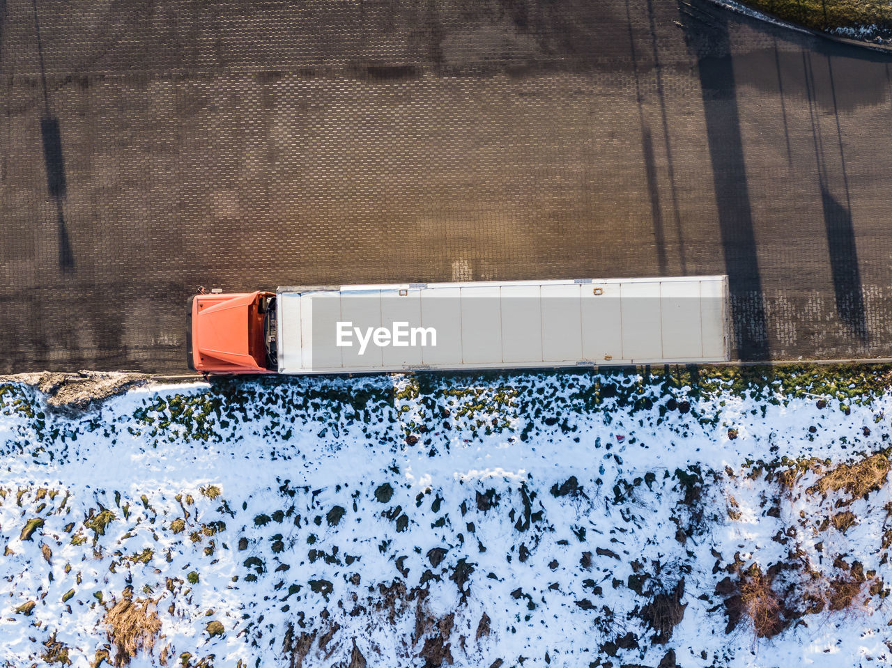 Aerial follow shot of white semi truck with cargo trailer attached through industrial warehouse