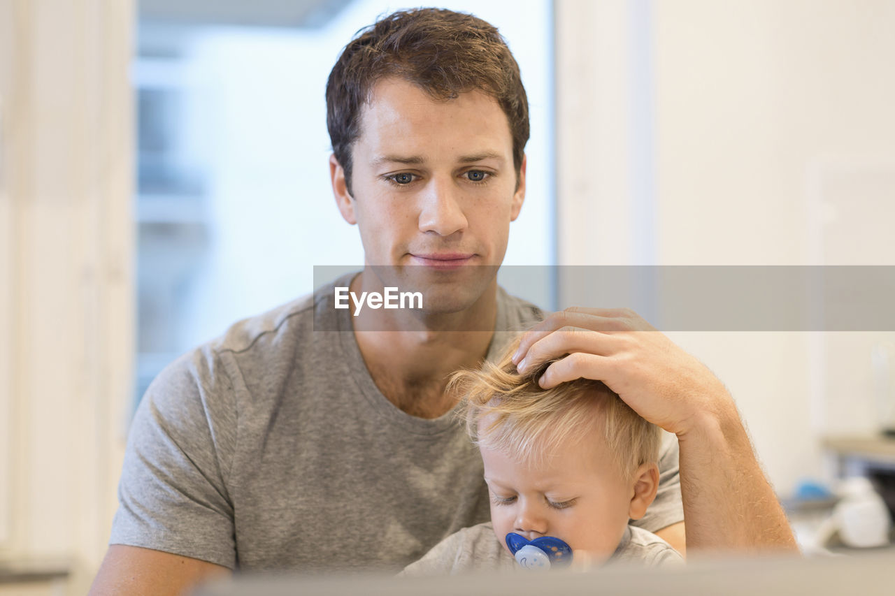 Baby boy sitting with father working on laptop in house