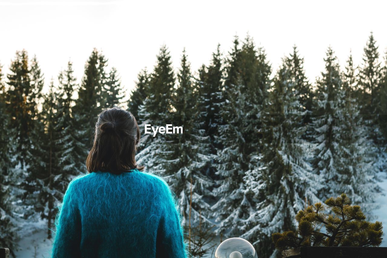 Rear view of woman standing against snow covered trees during winter