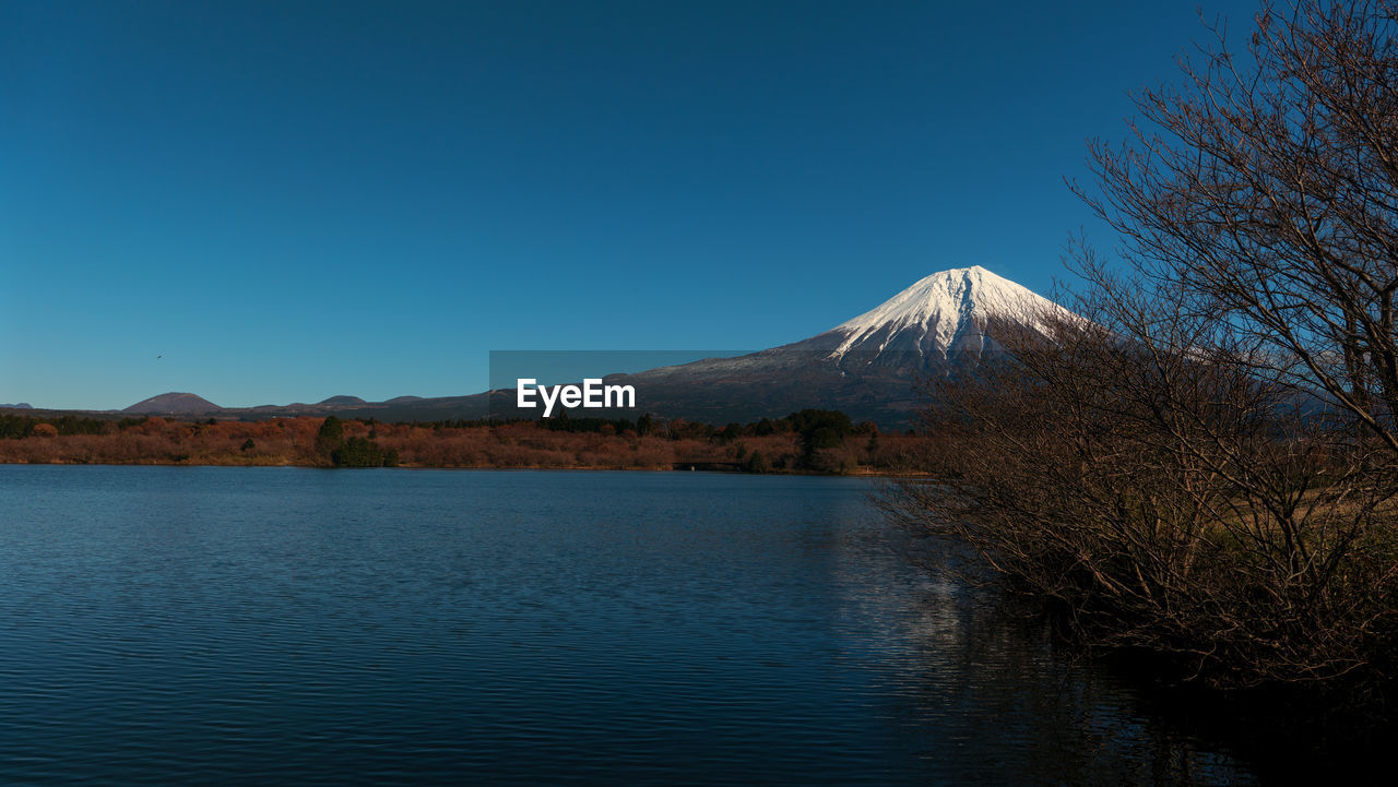 SCENIC VIEW OF LAKE BY MOUNTAIN AGAINST CLEAR BLUE SKY