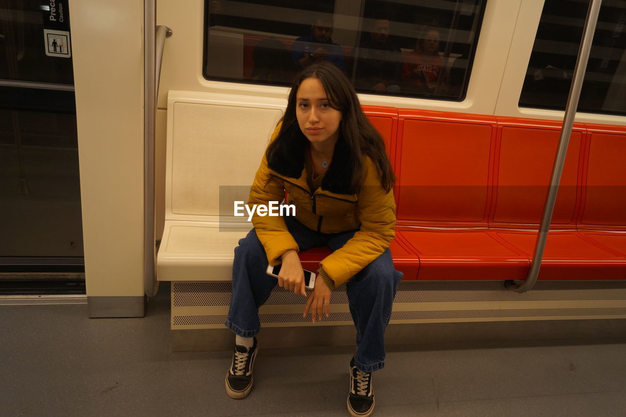 Full length portrait of young woman sitting inside of a train