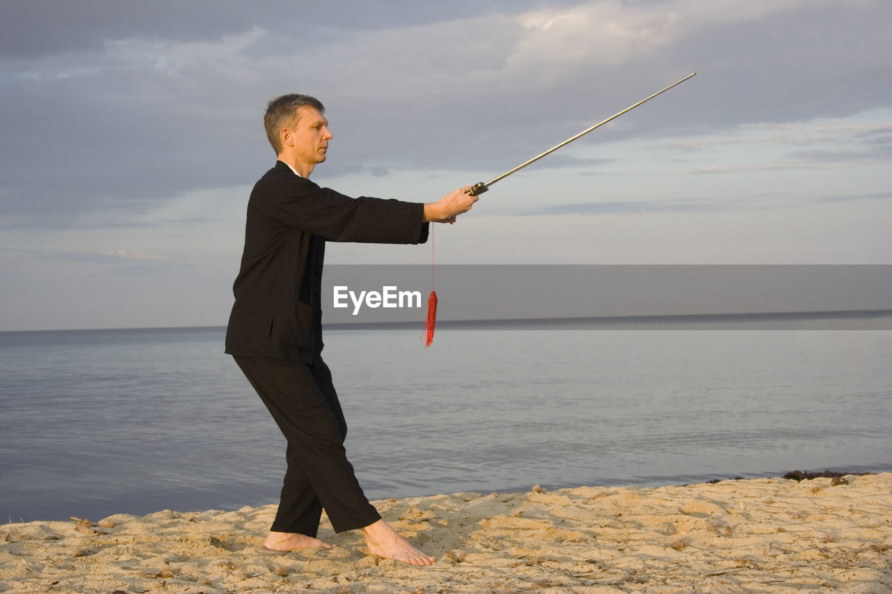 Man practicing tai chi at beach against cloudy sky