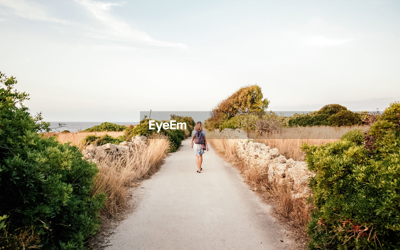 Rear view of woman walking on road against sky