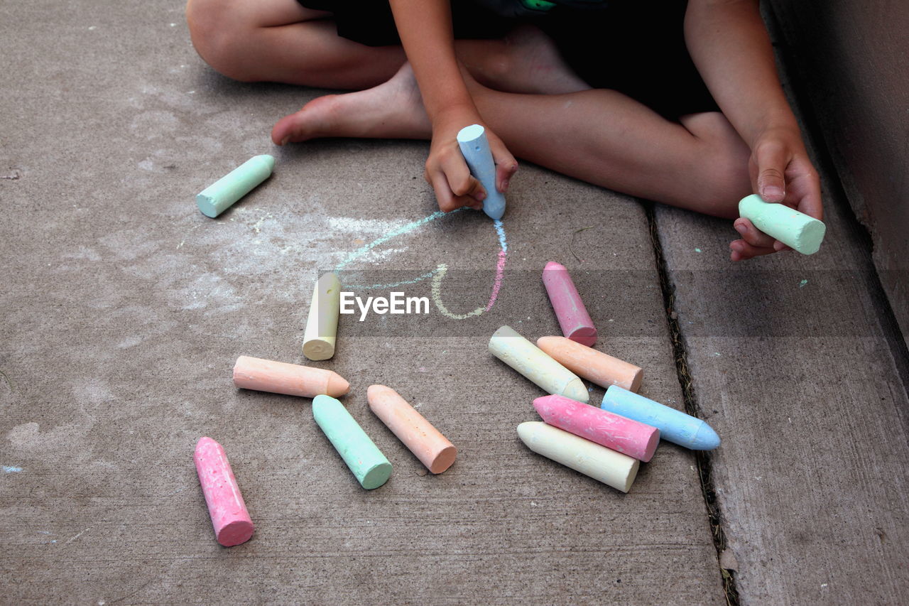 Low section of boy drawing heart shape with chalk on walkway