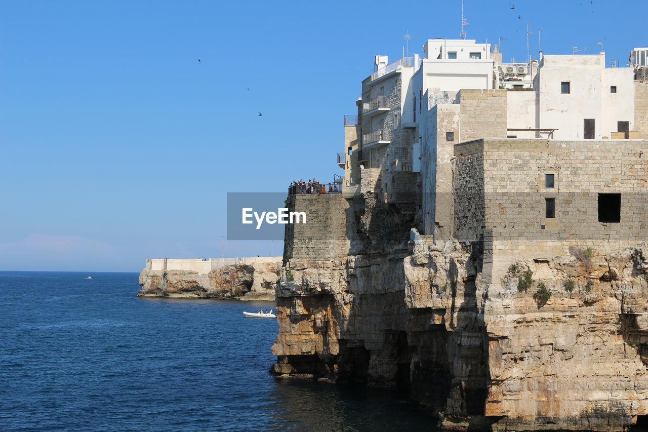 Buildings by sea against blue sky