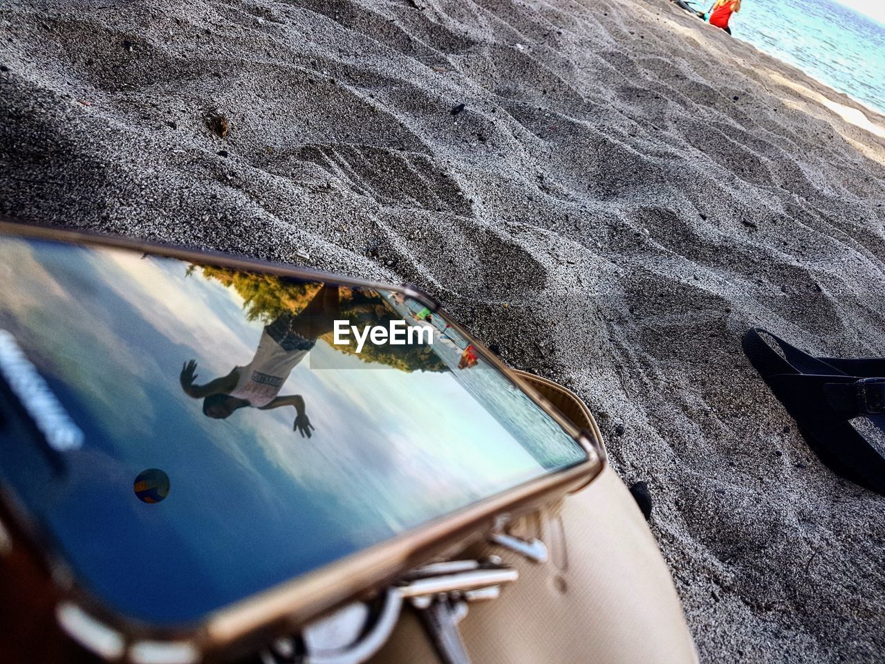 Reflection of woman on screen of mobile phone at sandy beach