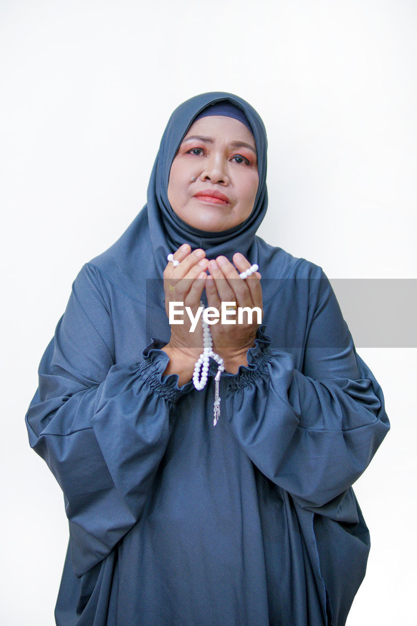 one person, studio shot, adult, portrait, clothing, white background, hijab, front view, indoors, religion, waist up, emotion, hood, young adult, cut out, outerwear, human face, person, women, headscarf, looking at camera, academic dress, standing, hand, belief