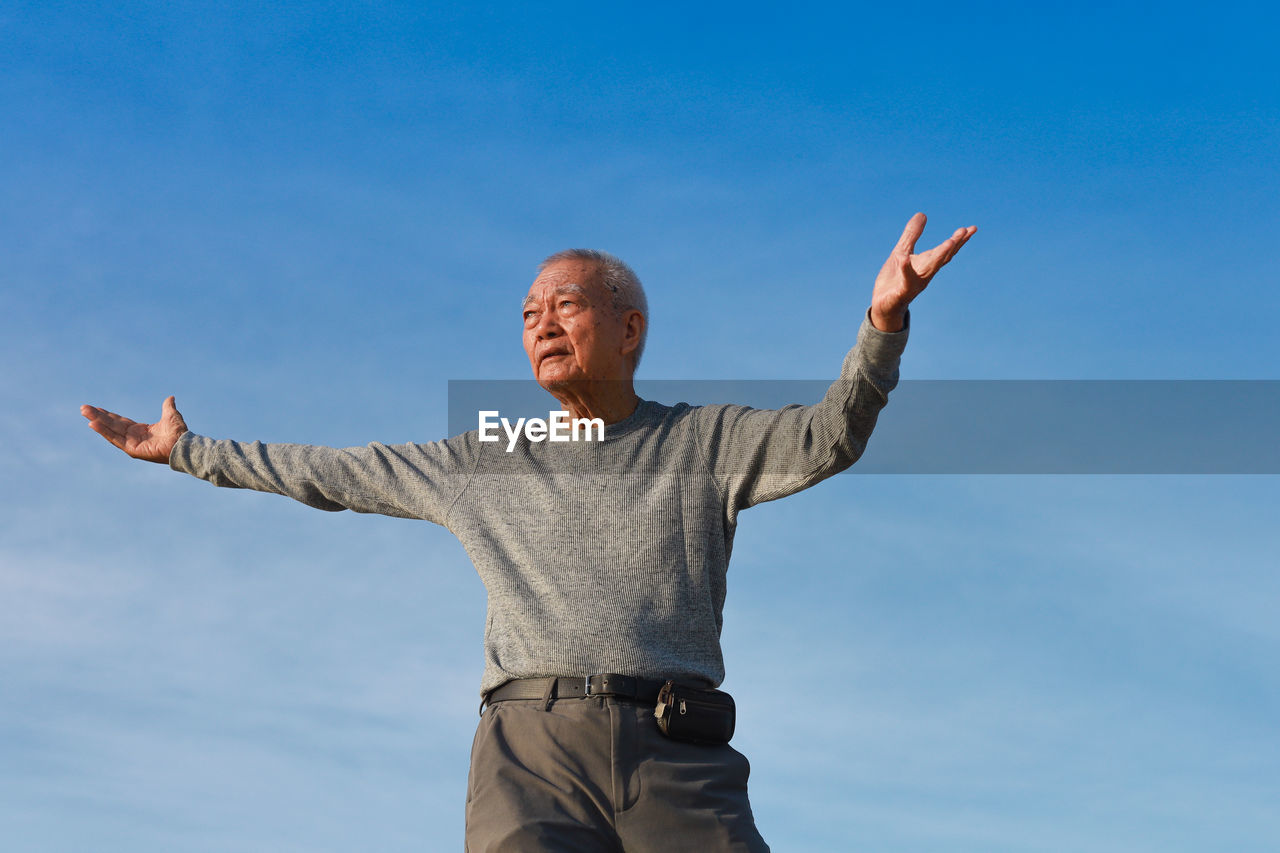 Low angle view of senior man standing against blue sky