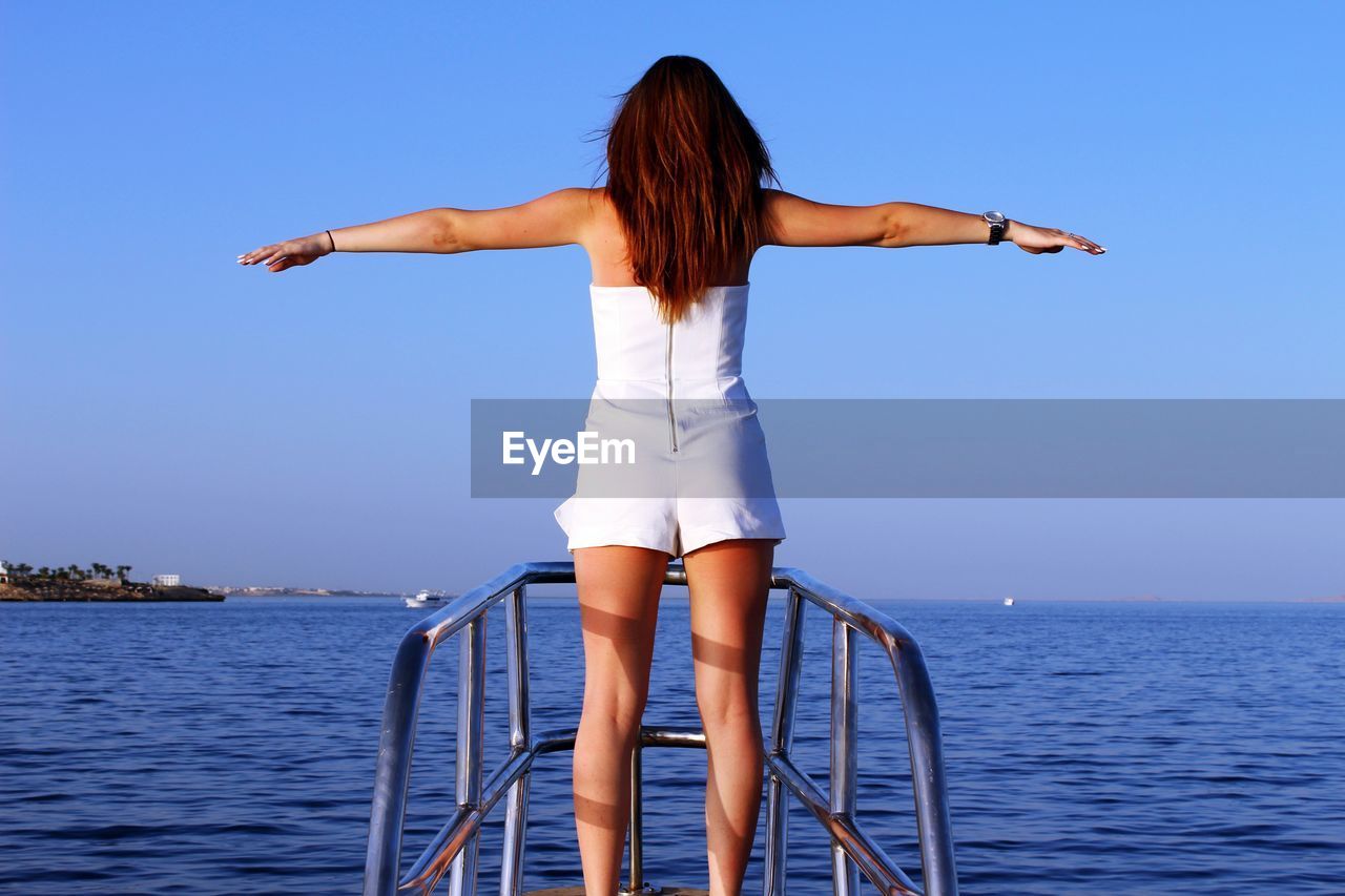 Rear view of woman with arms outstretched standing on jetty over sea