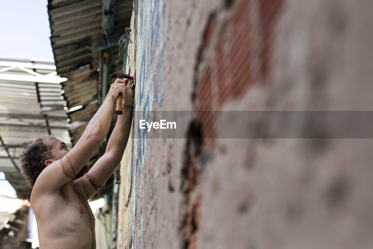 Side view of a shirtless man against the wall.