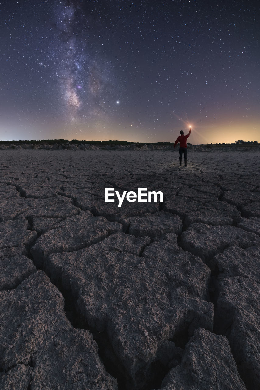 Tourist standing in rocky arid terrain with flashlight under starry sky at night