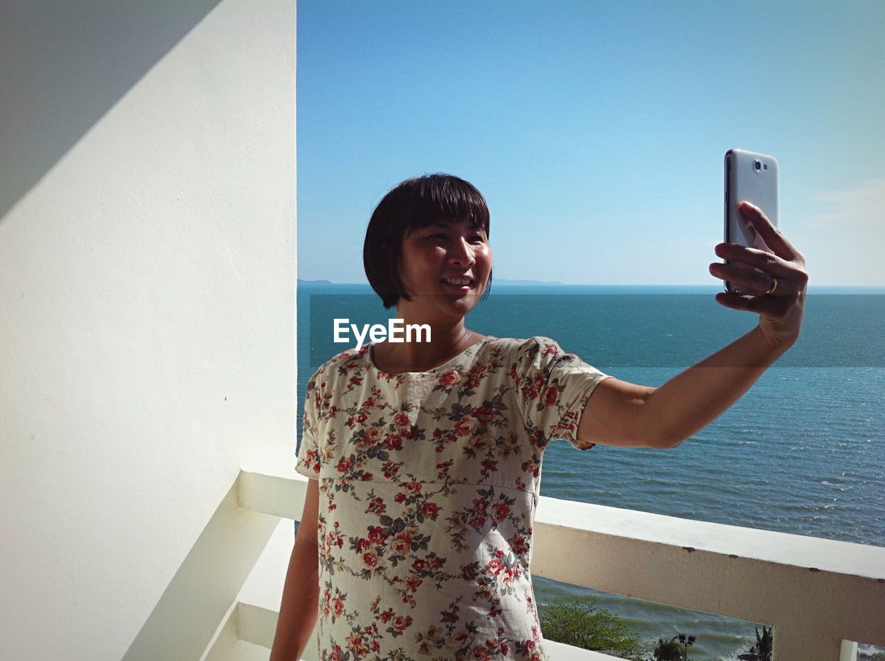 Happy young woman taking selfie against wall