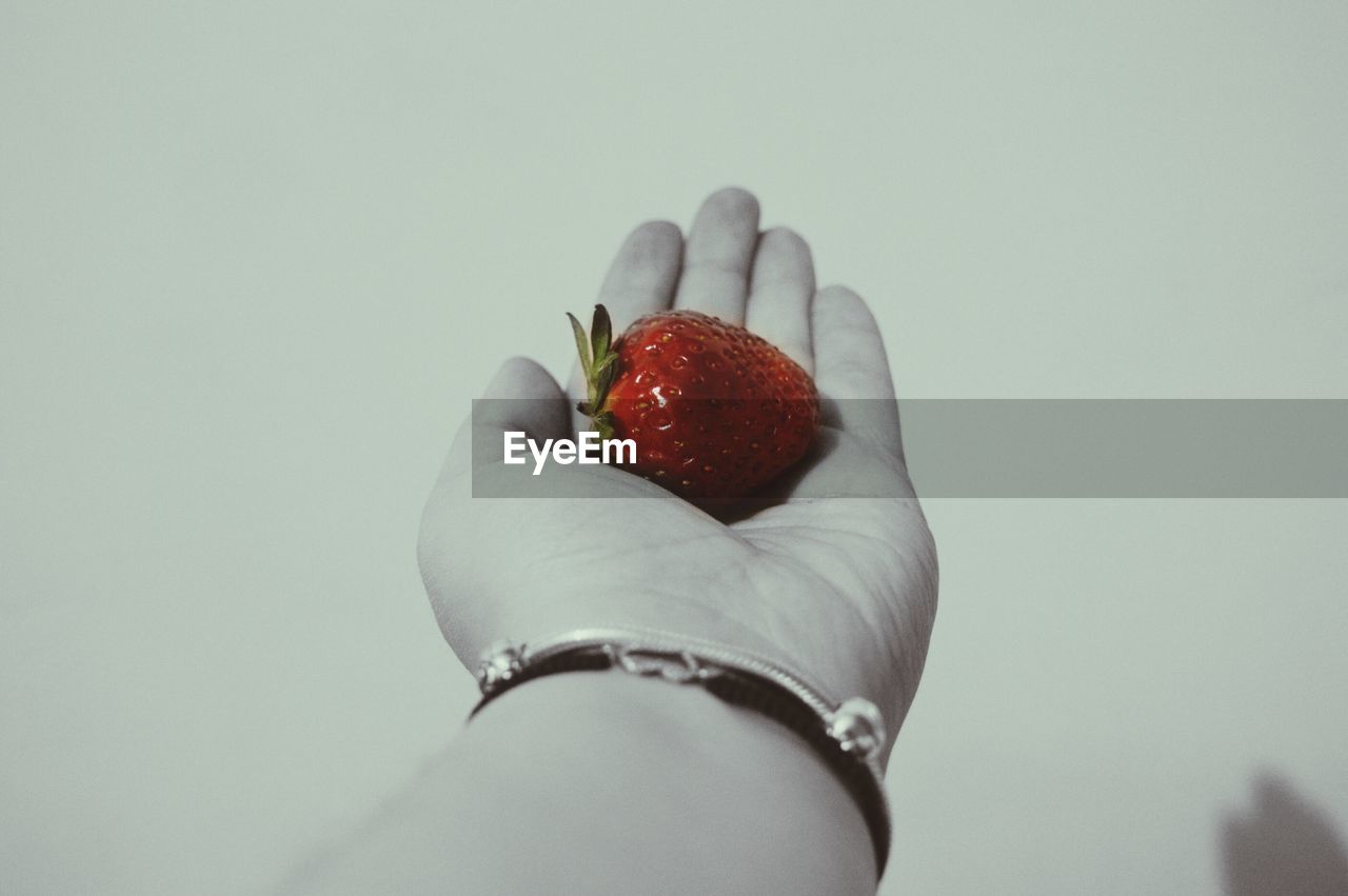 Cropped image of woman with strawberry on palm against white background