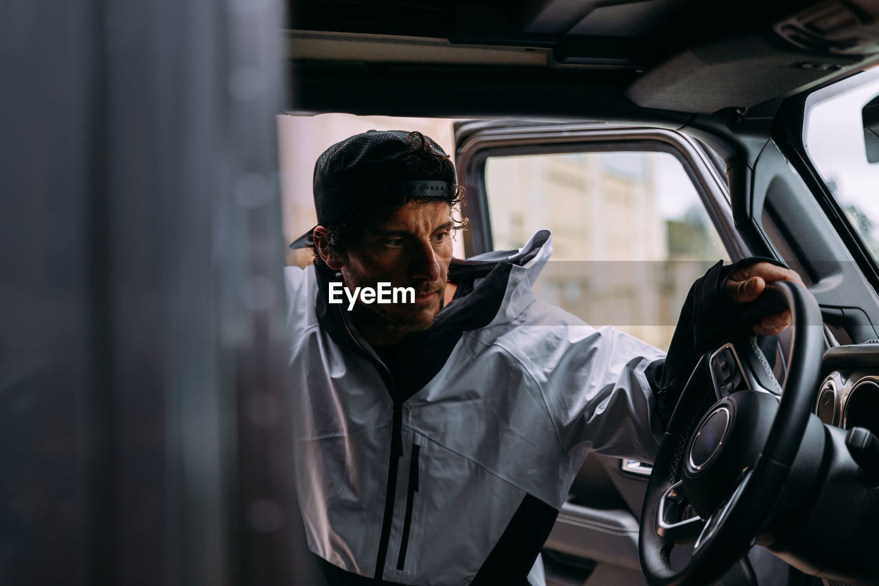 Side view of a man with cap and casual clothes getting into a car