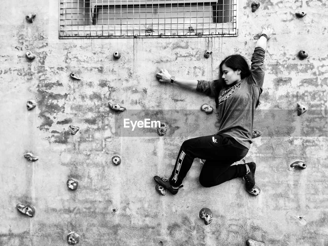 FULL LENGTH SIDE VIEW OF YOUNG WOMAN WITH ARMS RAISED AGAINST WALL