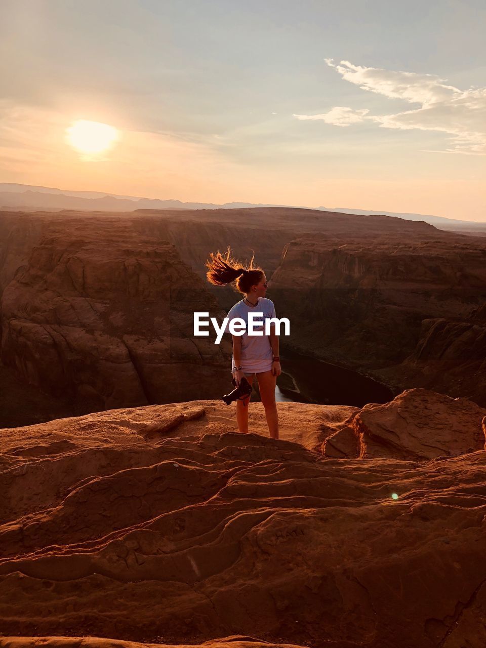 Woman tossing hair while standing on rock formation against sky during sunset