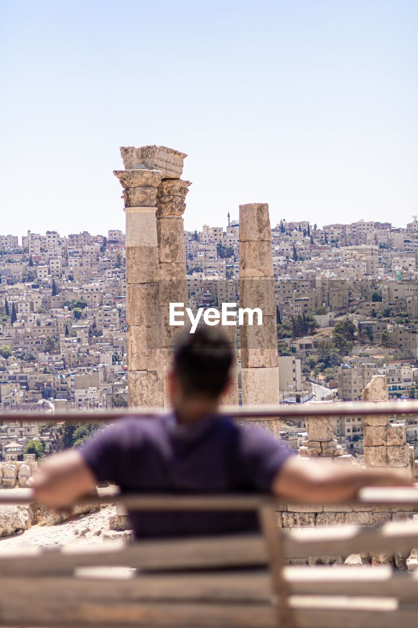 REAR VIEW OF WOMAN LOOKING AT CITYSCAPE AGAINST SKY