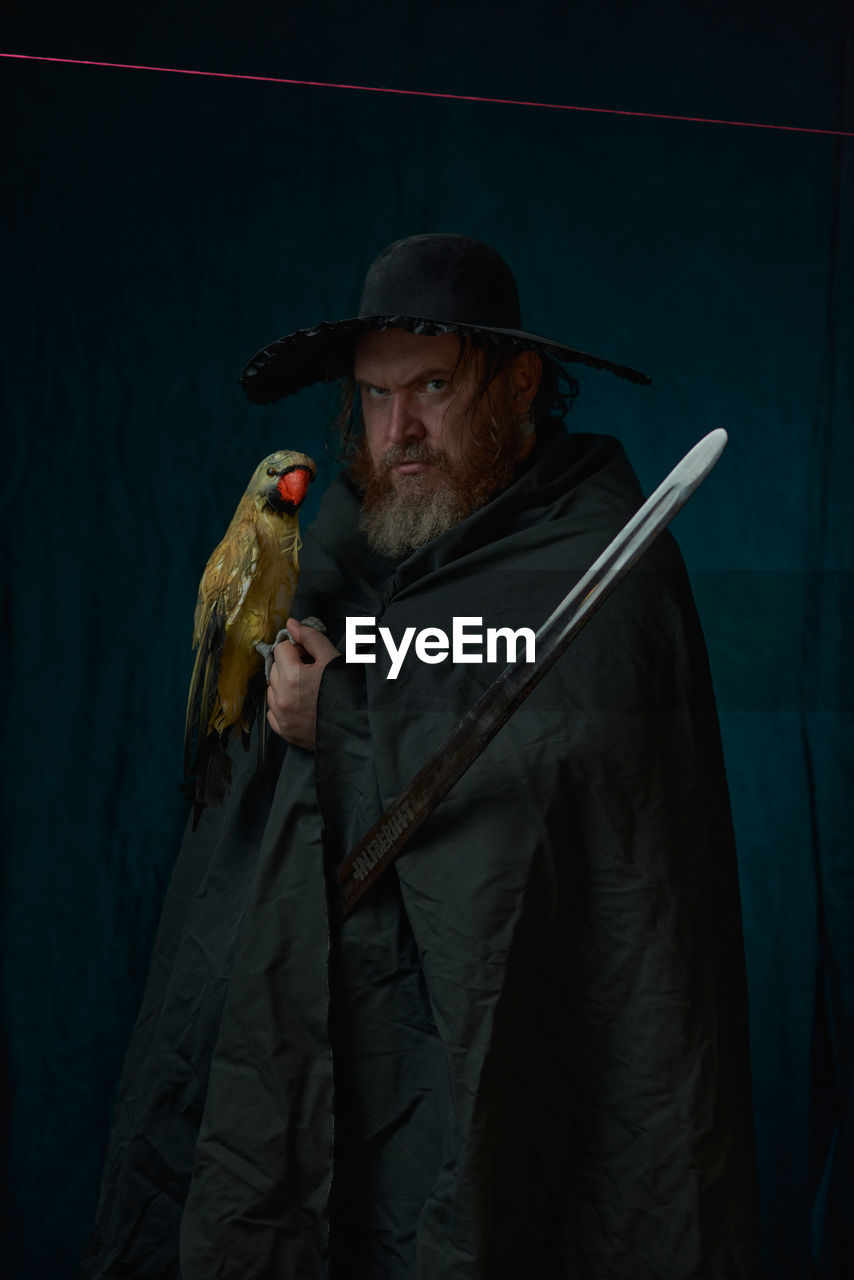 adult, one person, clothing, men, facial hair, person, holding, beard, bird, animal, screenshot, senior adult, weapon, waist up, mature adult, portrait, hat, standing, darkness