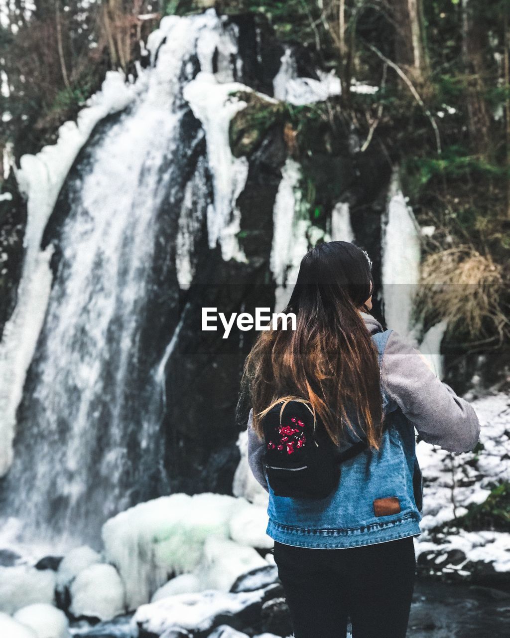 Rear view of woman standing against waterfall during winter