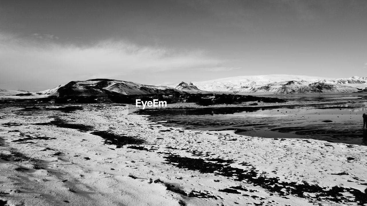 Scenic view of sea by snowcapped mountain against sky