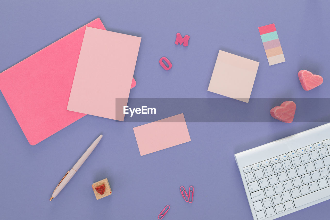 Office desk with keyboard, blank paper sheets, weekly planner, heart-shaped candies.