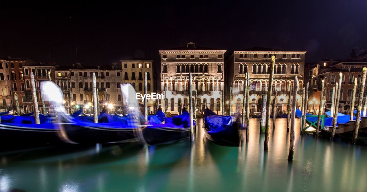 Gondolas moored in grand canal against illuminated buildings during night